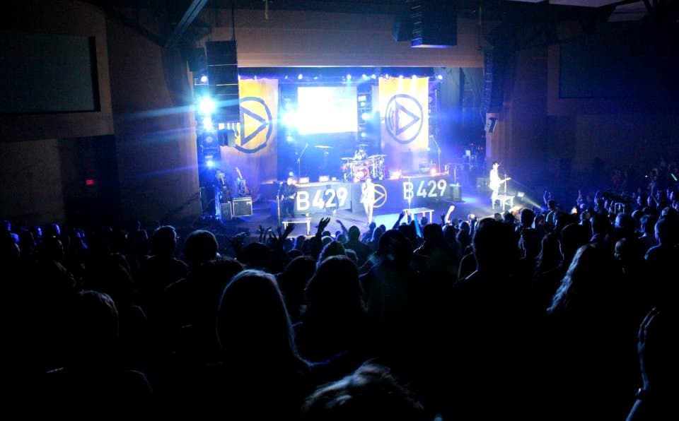 Wide shot of a Building 429 concert with the band on stage and a large audience in a theater under blue stage lighting