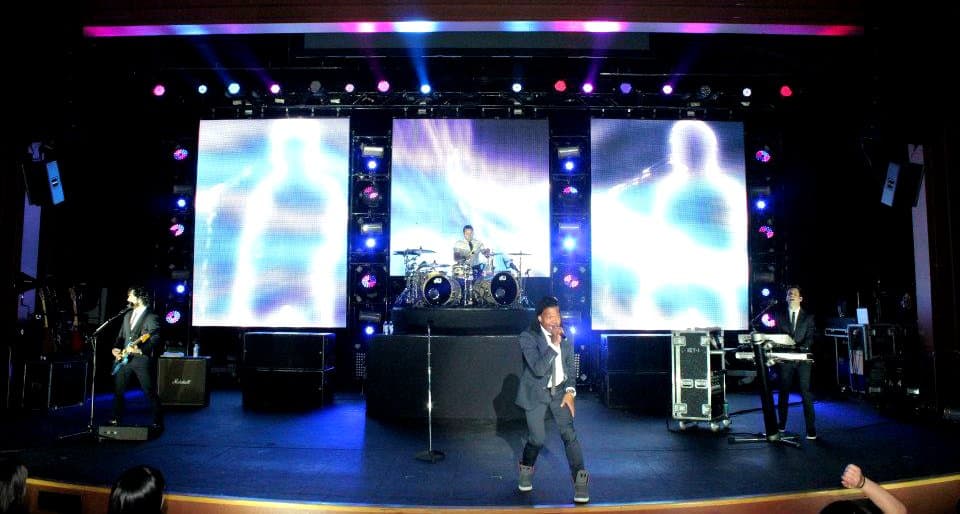 Band performing on a large indoor stage with massive LED screens and colorful stage lighting